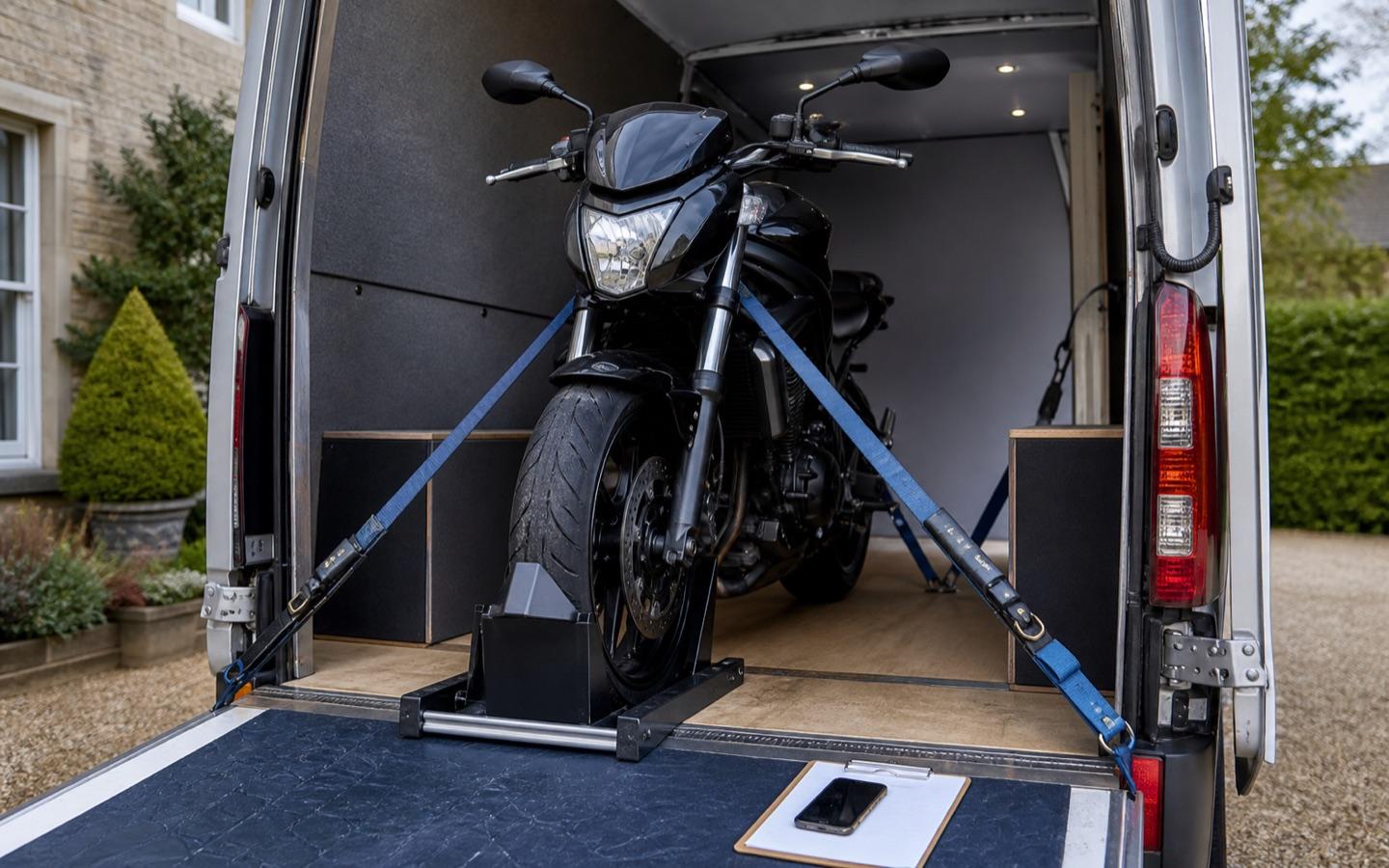 Motorbike secured with a wheel chock and soft straps inside an enclosed van
